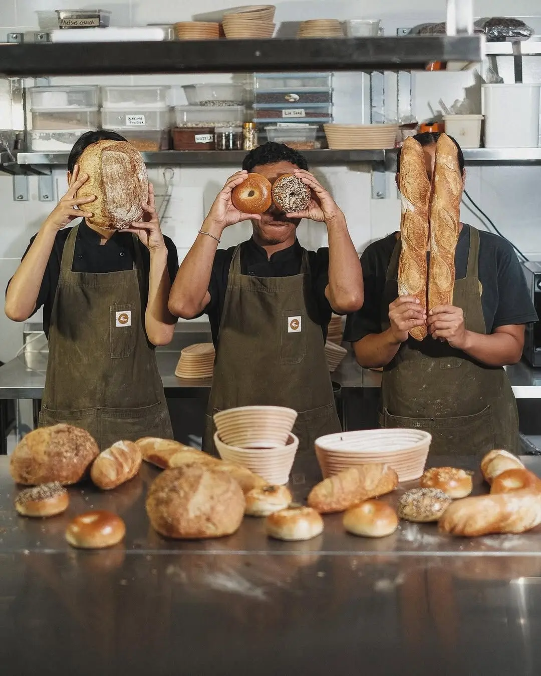 Three bakers posing with sourdough, bagel and baguettes in a commercial kitchen