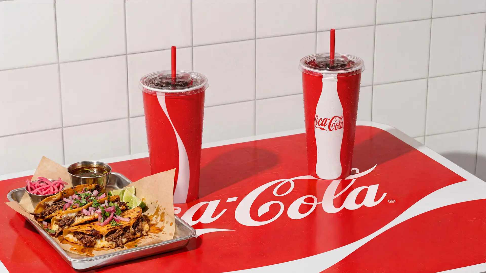Coca-Cola branded red tabletop with two fountain cups and tray of tacos