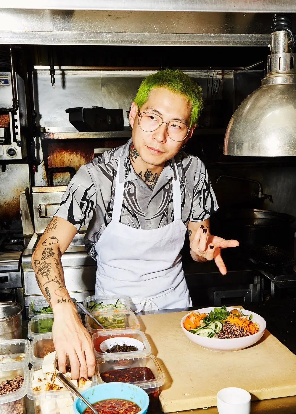 Neon-green-haired chef assembling grain bowl in stainless-steel kitchen