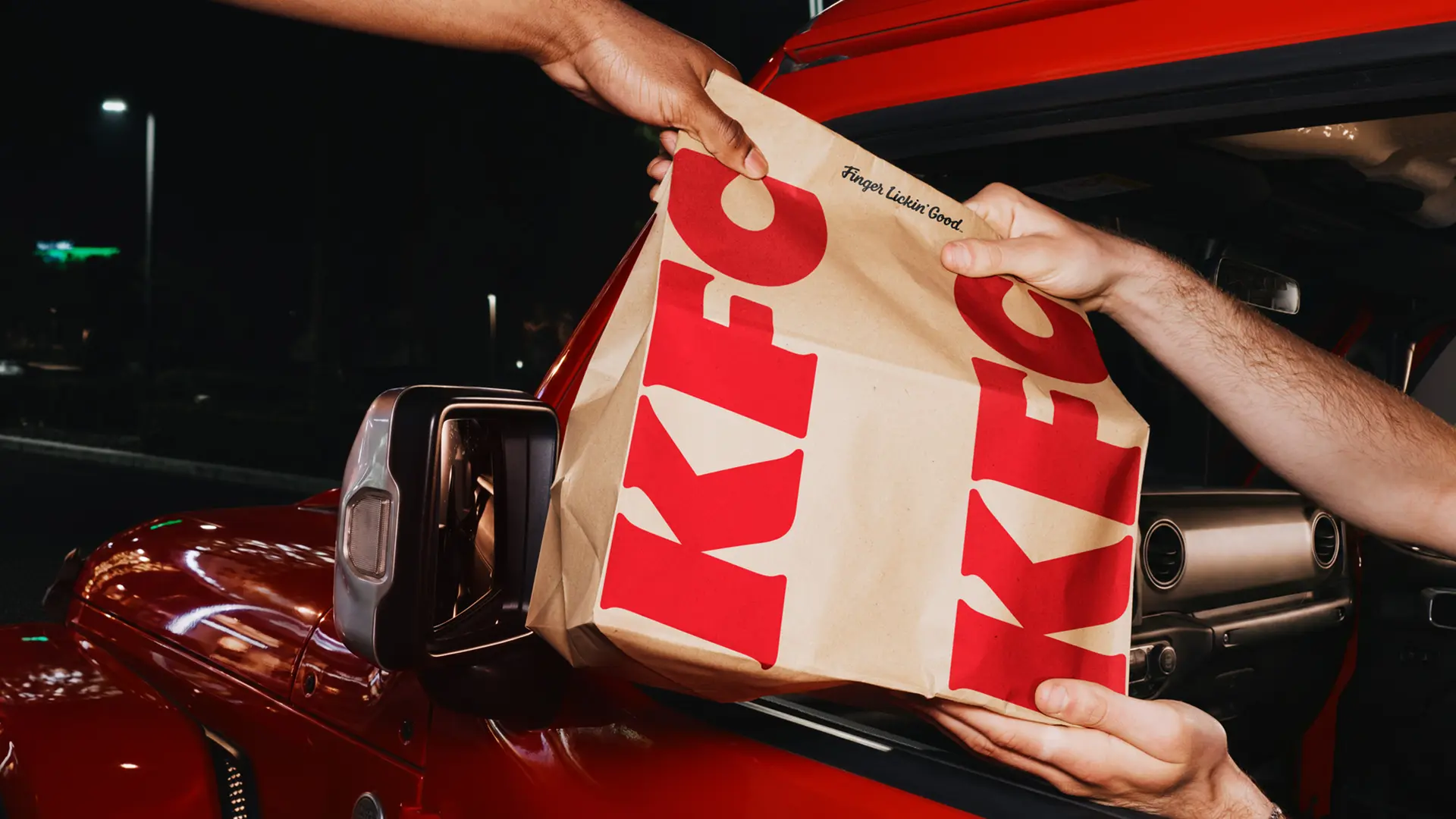 KFC kraft takeout bag handed through red car window at night