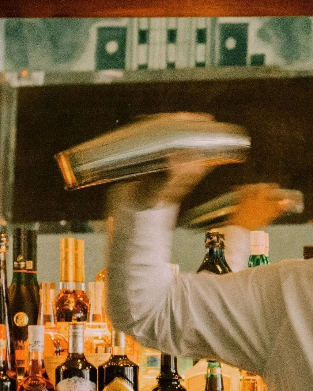 Bartender shaking stainless-steel cocktail shaker behind stocked back bar