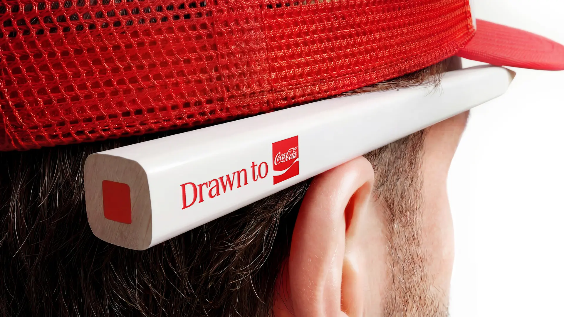 Coca‑Cola 'Drawn to' promotional pencil behind red trucker cap