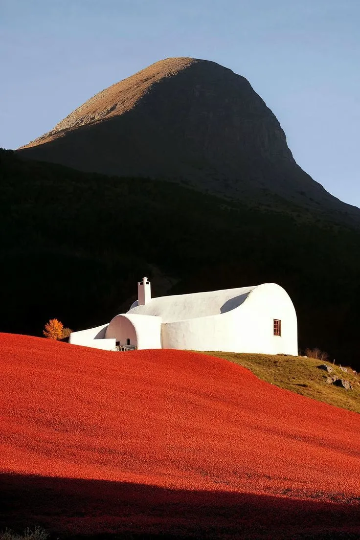 White stucco chapel above vivid red meadow with rounded mountain peak