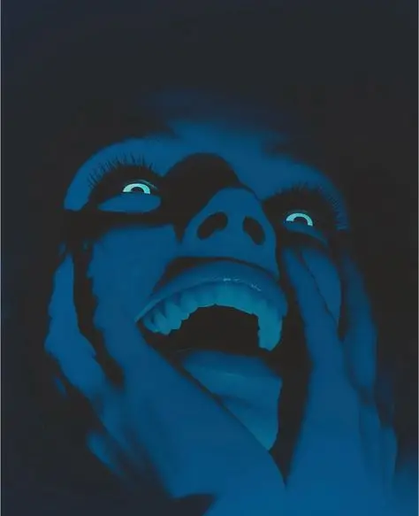 Blue-lit close-up portrait with black 'tear' paint and open mouth
