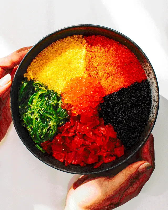 Overhead bowl of segmented seafood roe, seaweed and red pickles