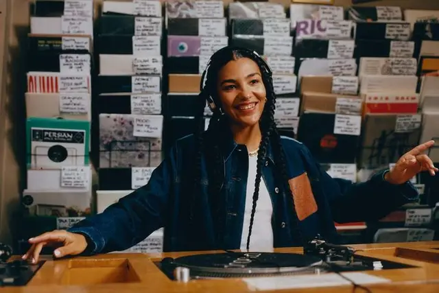 Record-store DJ at turntable surrounded by labeled vinyl crates