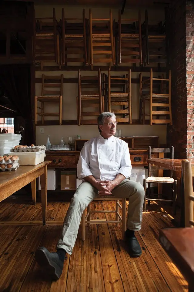Chef in rustic prep room with stacked wooden ladder-back chairs and egg crates