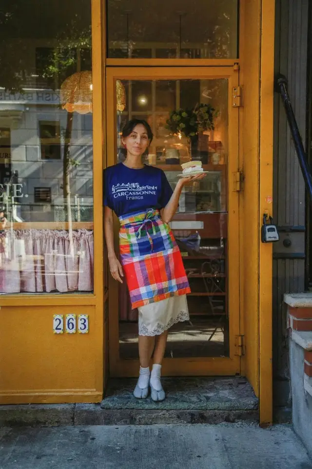 Woman holding cake at mustard-yellow bakery doorway (263)