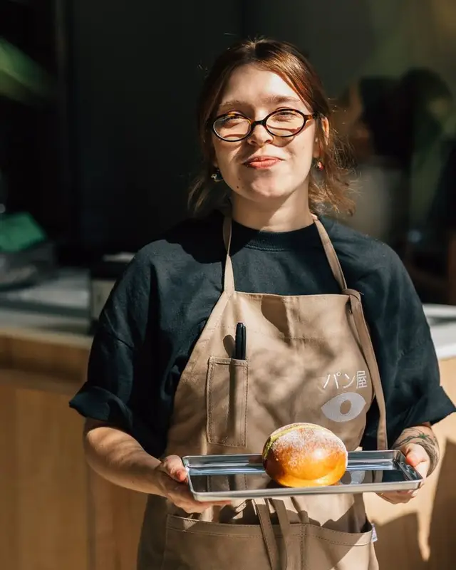 Bakery staff in beige apron presenting powdered bun on stainless tray