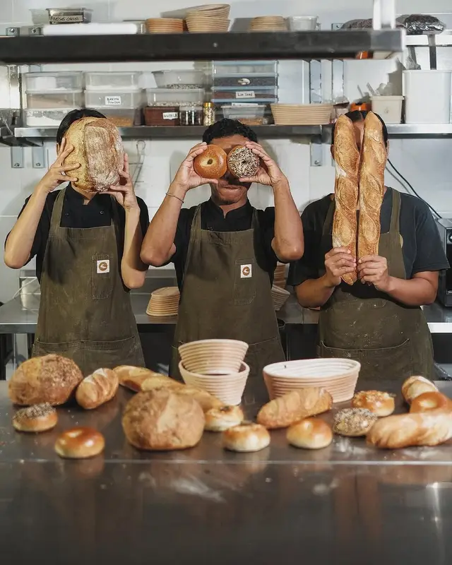 Three bakers posing with sourdough, bagel and baguettes in a commercial kitchen