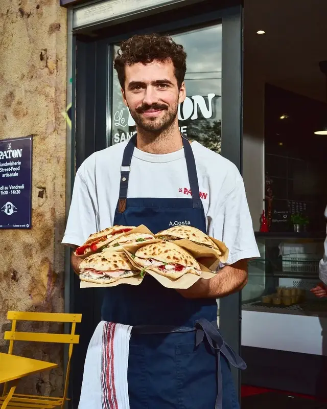 Server holding folded flatbread sandwiches outside Le PAPON sandwich shop