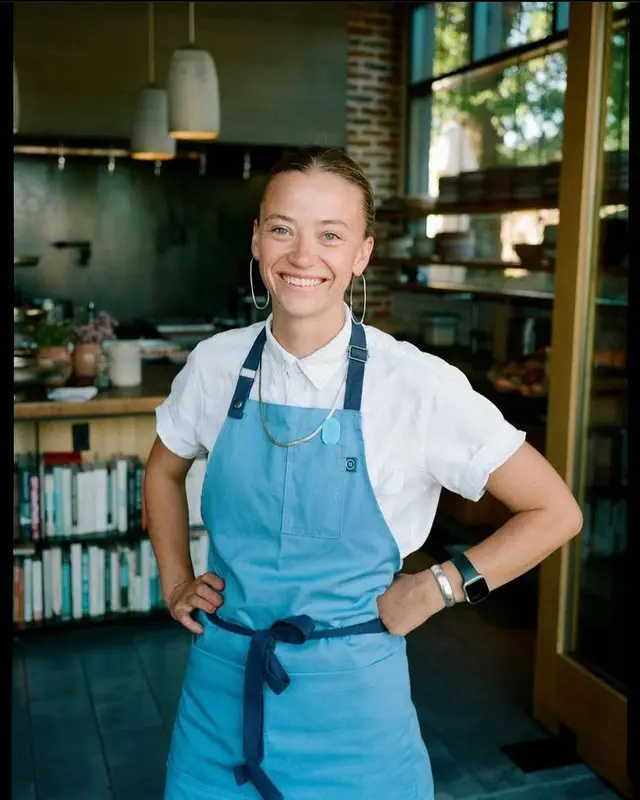 Smiling barista in light blue apron inside neighborhood café