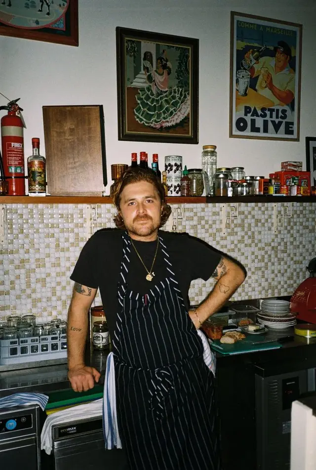 Chef in pinstripe apron at tiled kitchen counter with vintage posters