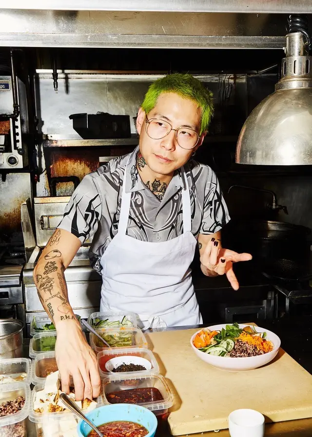 Neon-green-haired chef assembling grain bowl in stainless-steel kitchen