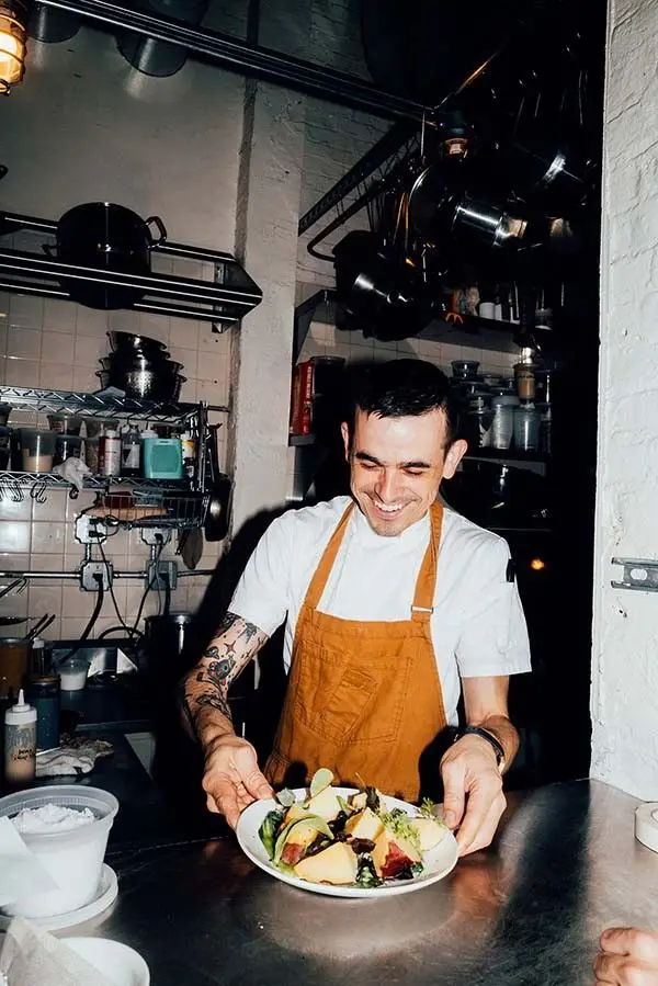 Chef plating a salad in a small commercial kitchen, orange apron