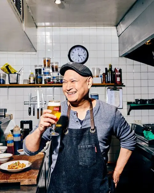 Chef raising a beer in a tiled commercial kitchen