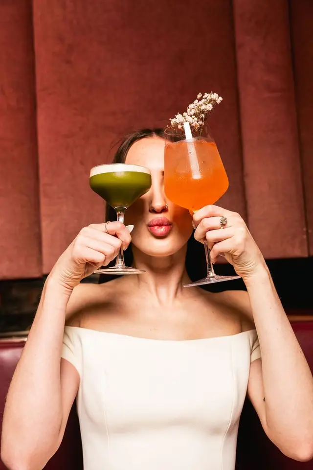 Editorial portrait: green foam coupe and orange spritz in velvet booth