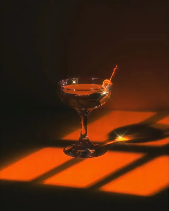 Orange-lit coupe cocktail with garnish and window-grid shadow