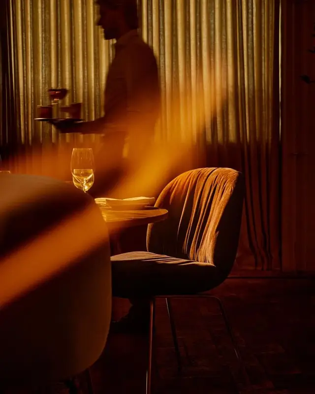 Velvet dining chair and waiter silhouette in warm amber restaurant light
