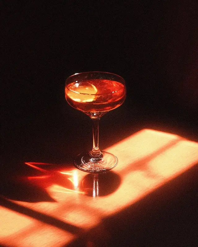 Coupe glass with amber cocktail and lemon twist in warm window light