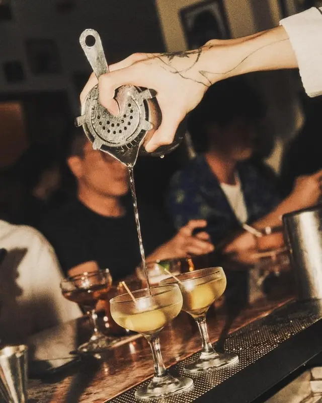 Pouring cocktails through metal strainer into coupe glasses