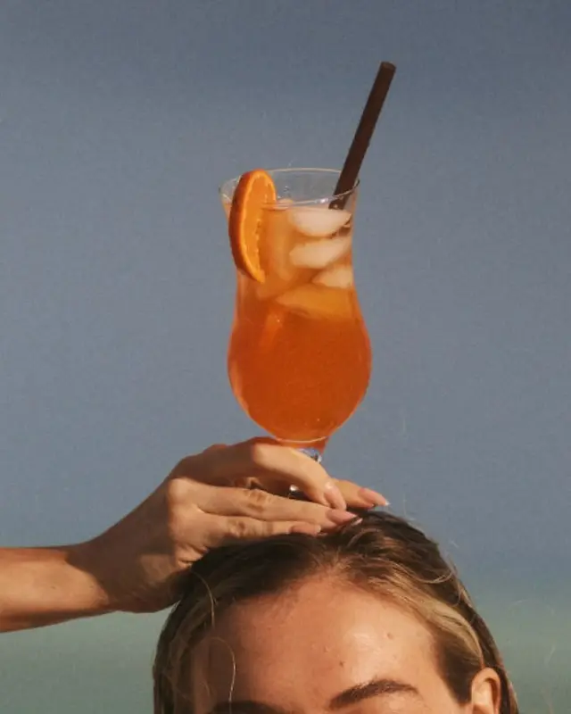 Orange cocktail balanced on person's head against blue sky