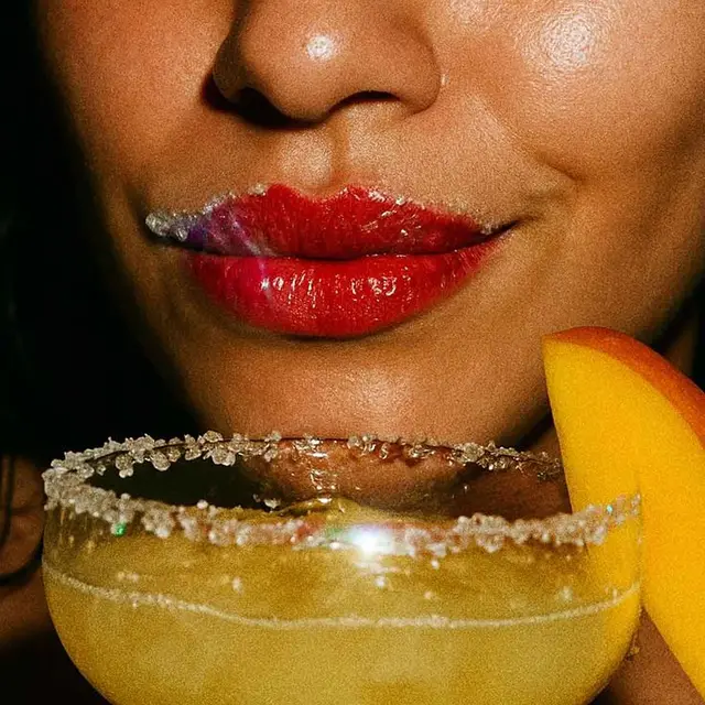 Close-up glossy red lips smoking beside peach-garnished sugar-rim cocktail