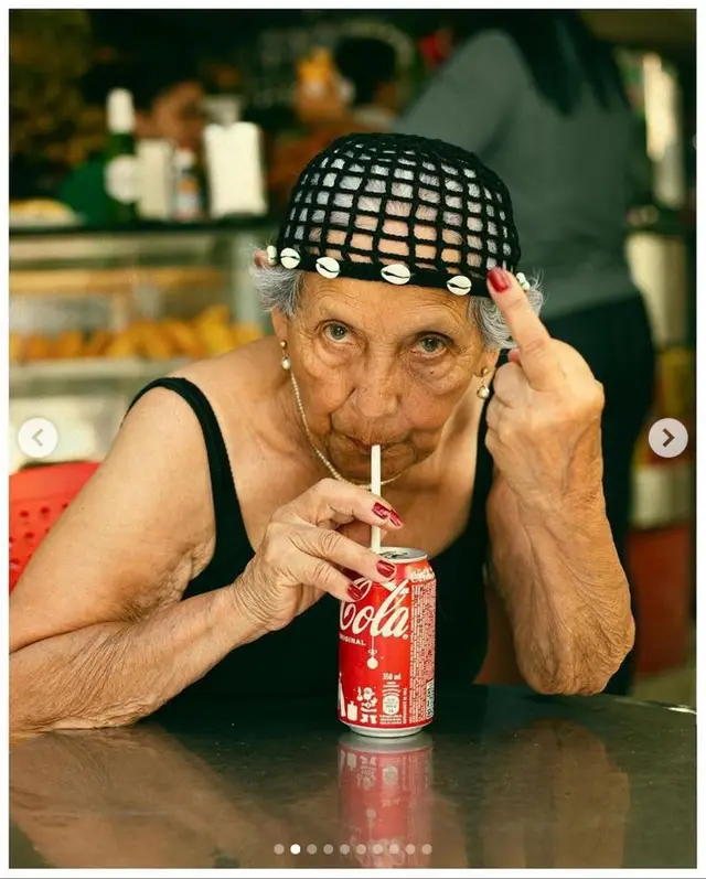 Elderly woman sipping Coca‑Cola and giving middle finger — candid market portrait
