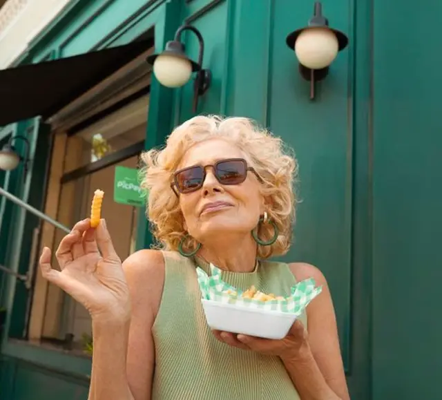 Mature woman eating crinkle-cut fries at teal storefront