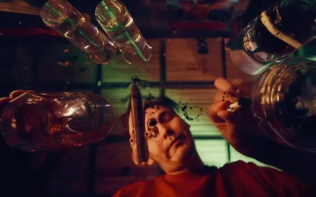 POV under-counter: man sprinkling grounds onto open-faced snack surrounded by glass jars