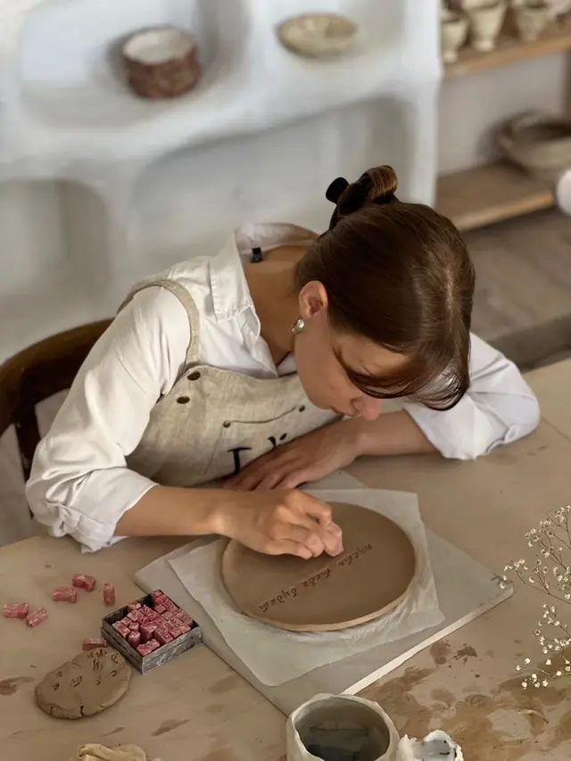 Artist carving lettering into leather-hard ceramic plate in sunlit studio
