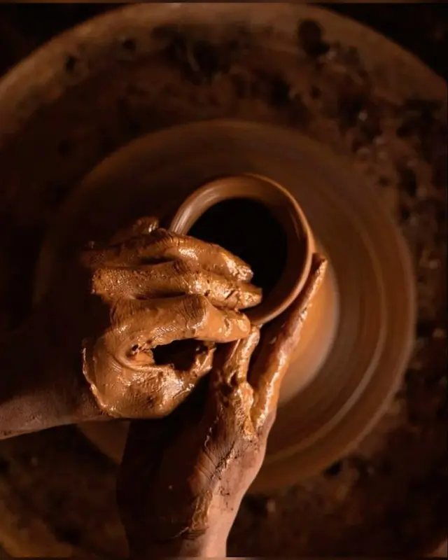 Hands shaping a wheel-thrown terracotta pot — close-up