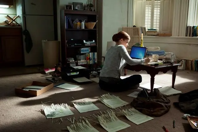 Sunlit apartment scene: person sorting papers and white strips on floor with laptop
