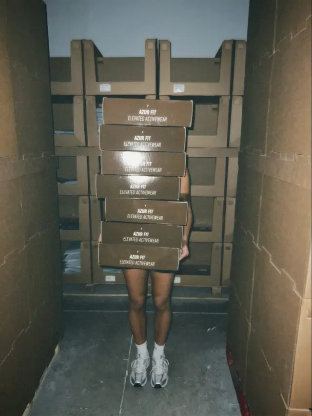 Person Hidden Behind Stack of 'AZUR FIT Elevated Activewear' Boxes in Warehouse