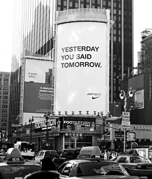 Nike billboard reading "YESTERDAY YOU SAID TOMORROW." above Footaction storefront — black‑