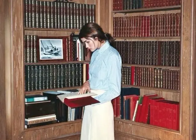Woman reading a red hardcover in a wood‑paneled home library