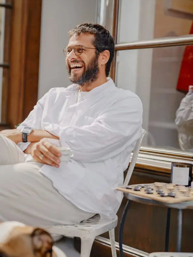 Laughing man in white linen shirt with espresso and wooden game board