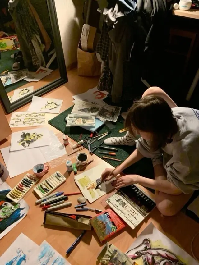 Artist working on the floor with scattered watercolors and pastels