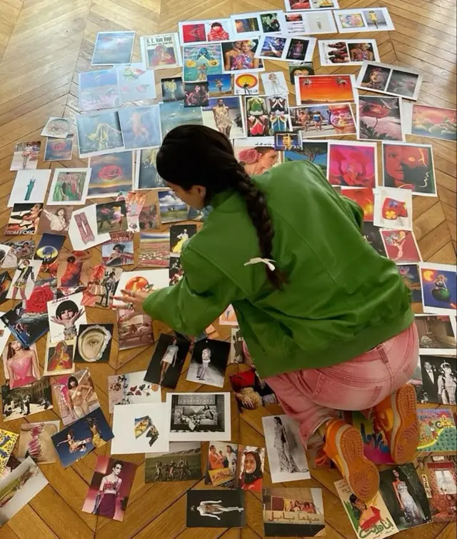 Overhead view: person arranging colorful fashion and art clippings on herringbone wood flo
