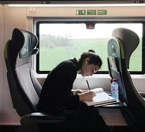 Passenger writing in notebook on train with green countryside outside