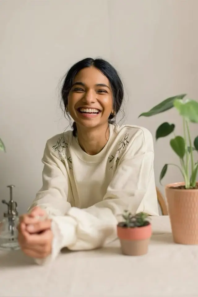 Smiling woman in cream embroidered sweatshirt with potted plants — lifestyle portrait