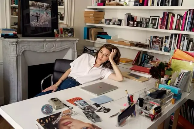 Person reclining at a white desk in a home creative studio with MacBook and bookshelves