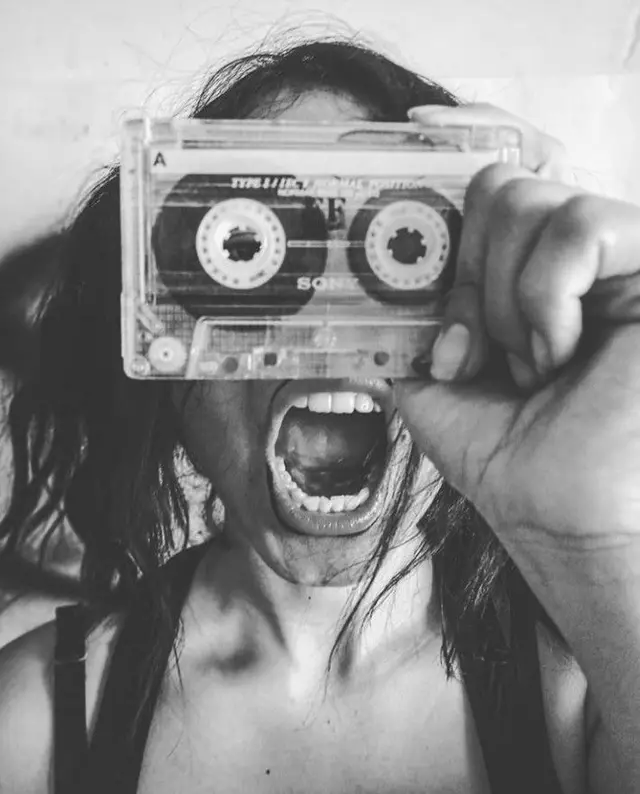 Black-and-white portrait holding transparent Sony cassette over face