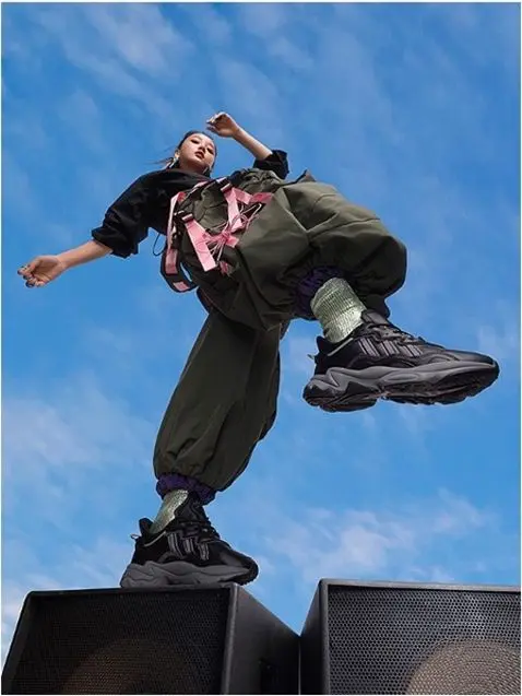 Low-angle streetwear shot — chunky black sneakers, olive cargo pants, pink backpack