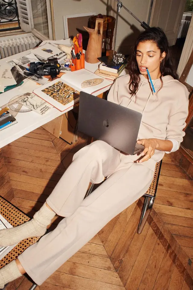Casual creative in beige loungewear working on a MacBook in a cluttered home studio
