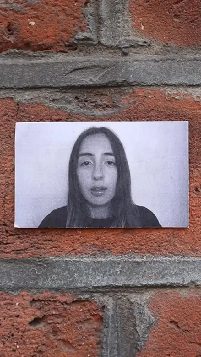 Black-and-white photocopy portrait paste-up on red brick wall