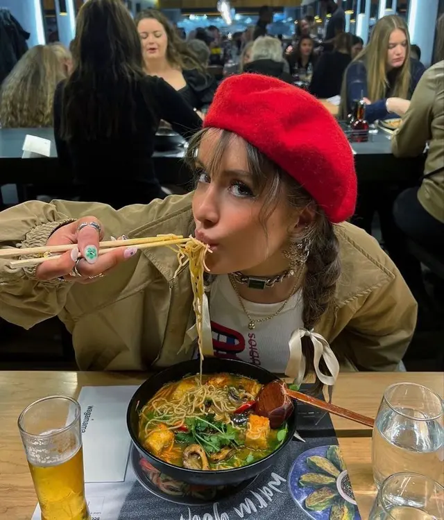 Person in red beret slurping ramen at crowded restaurant
