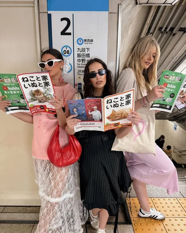 Three women on Tokyo Tozai Line platform reading Japanese pet magazines