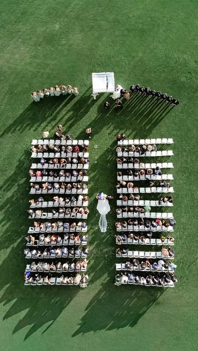 Aerial view — outdoor lawn wedding with white canopy and central aisle