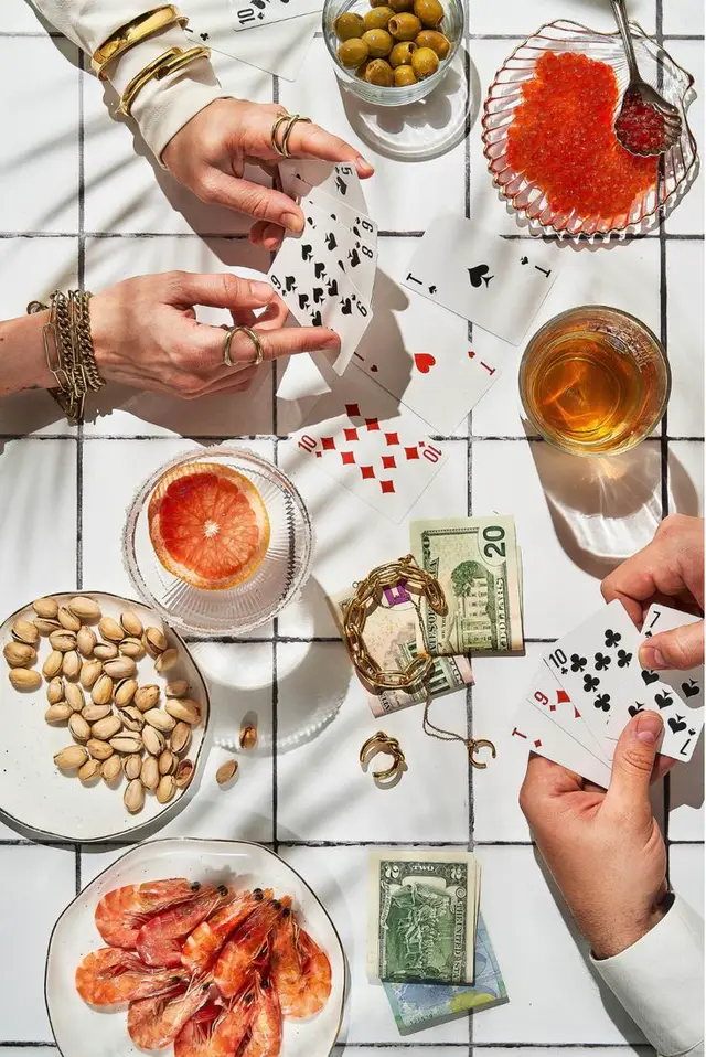 Overhead card game flatlay with shrimp, caviar, pistachios and whiskey